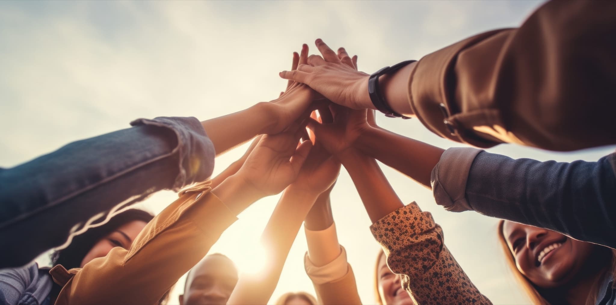 A group of friends joining hands together in a high five against a bright sky