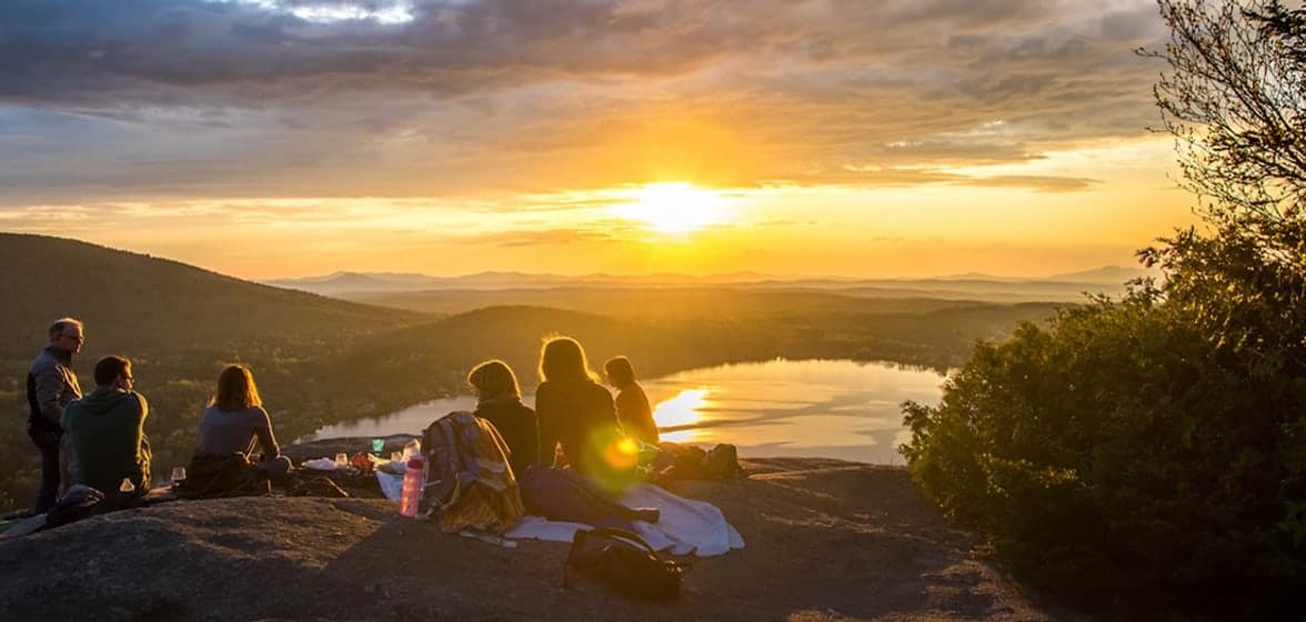 A group of travellers watching the sunset over a lake from a hilltop